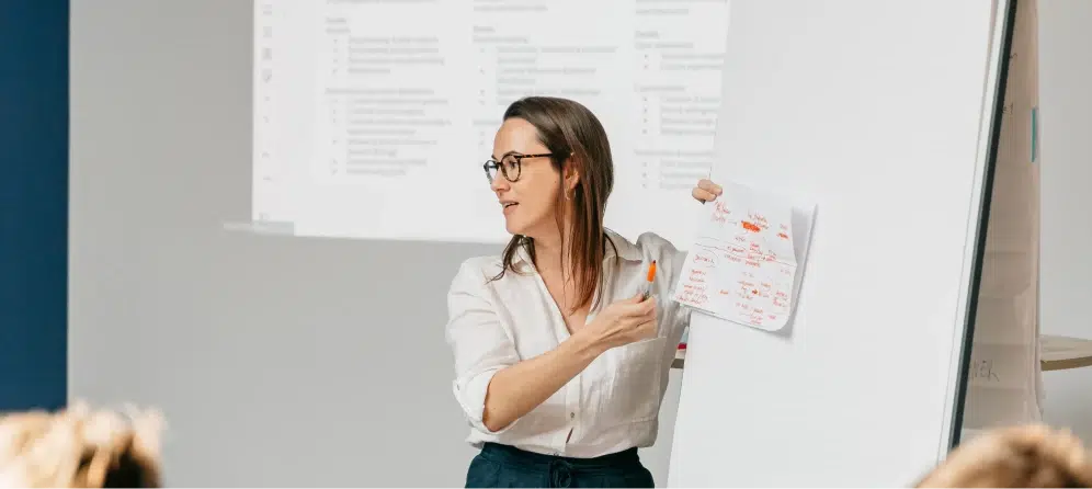 A professional explaining AI ethics and compliance concepts on a whiteboard, representing AI governance, transparency, and responsible implementation.